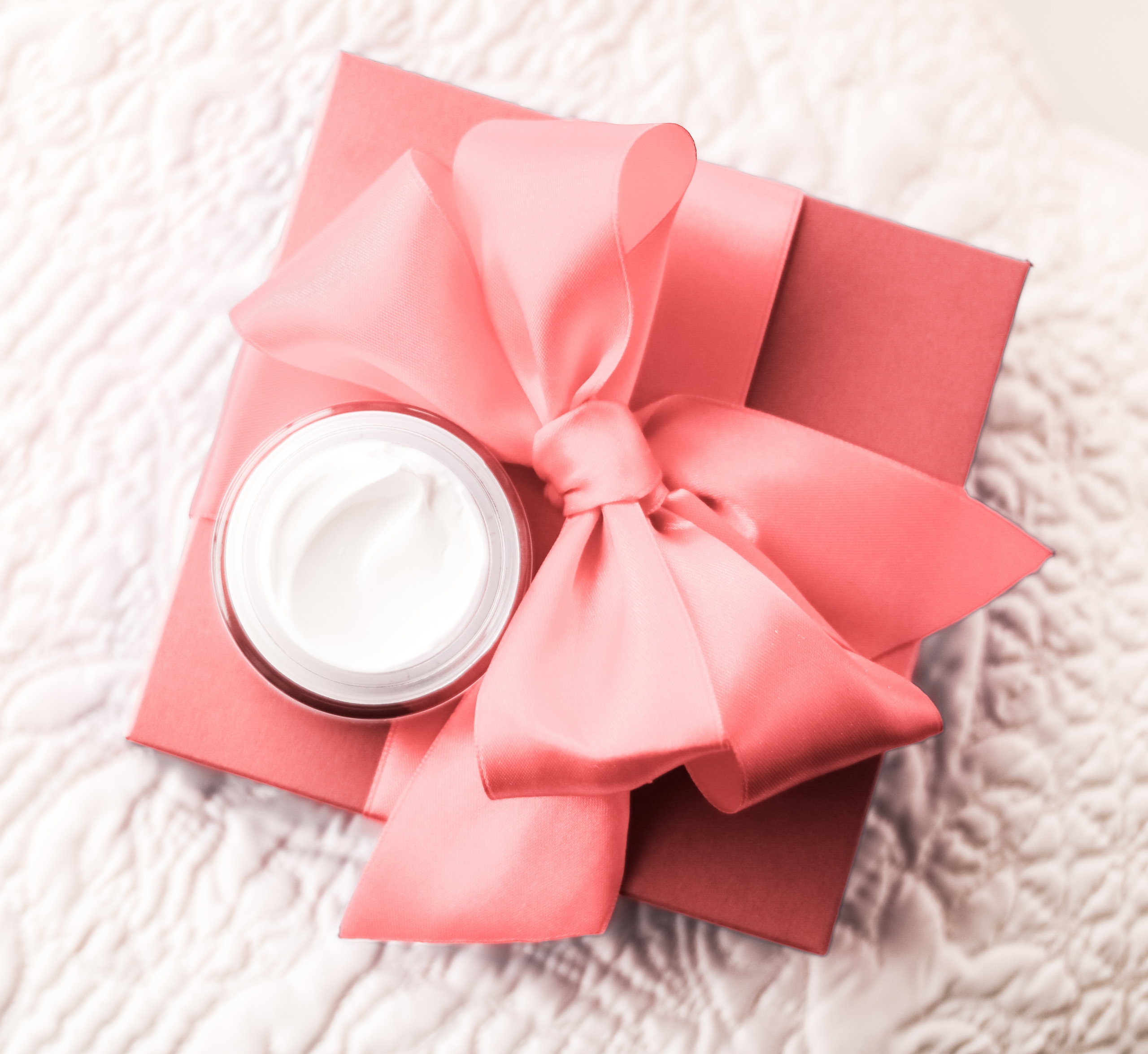 Pink Gift box with a Pink bow and white cream spa product sitting on quilted white fabric